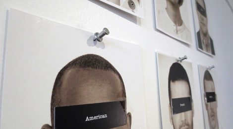 black and white portraits pinned to the wall, with their eyes covered by pieces of black card with national labels